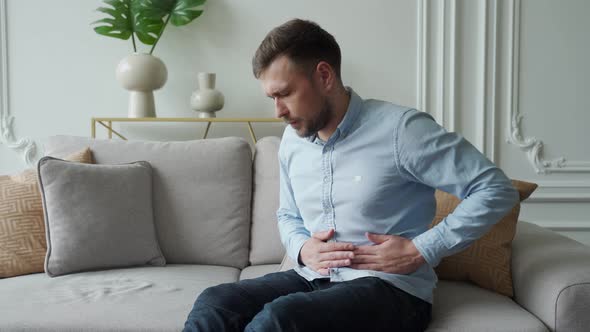 A Man Suffers From Abdominal Pain While Sitting at Home on the Couch alt