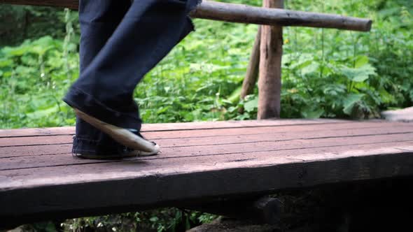A girl in wide dark pants crosses a river on a wooden bridge in the woods in slow motion