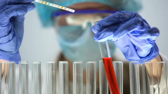 Researcher Measuring pH Level in Red Liquid Substance With Litmus Paper, Test alt