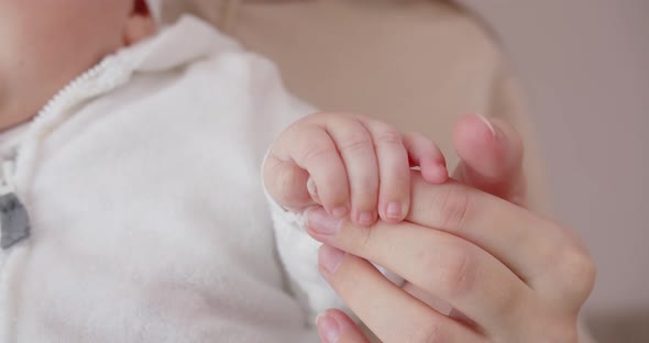 A Newborn Baby Holds A Mother's Finger With Her Little Pen. Mom Gently Strokes The Baby's Little Pen
