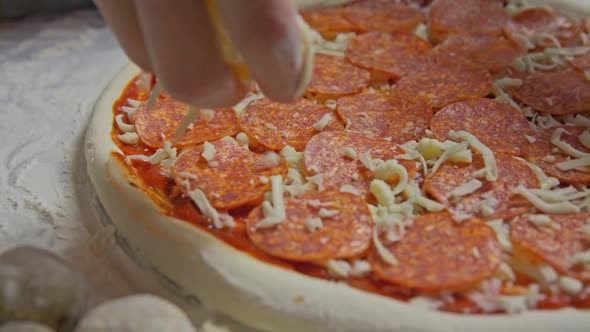 Professional Chef Pours Grated Cheese Onto a Pizza Base with Tomato Paste on the Table Decorated alt