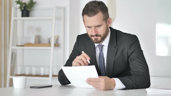 Pensive Businessman Reading Documents in Office, Paperwork alt