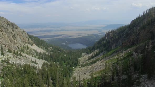 Camera flies over a mountainside valley with a lake at the base alt