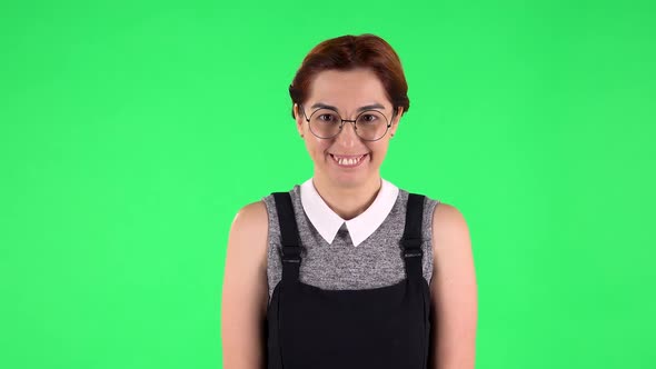 Portrait of Funny Girl in Round Glasses Is Laughing Shyly While Looking at Camera. Green Screen alt