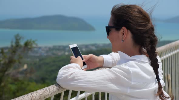 Young Woman Types on Phone Leaning on Viewpoint Handrails alt