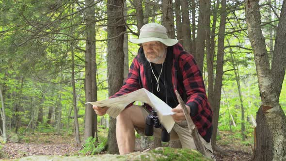 An older man looking at a map while hiking in a scenic forest in the mountains alt