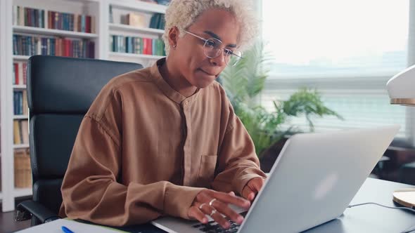 Young African American Woman Freelancer Works Using Laptop Sits at Office Desk alt