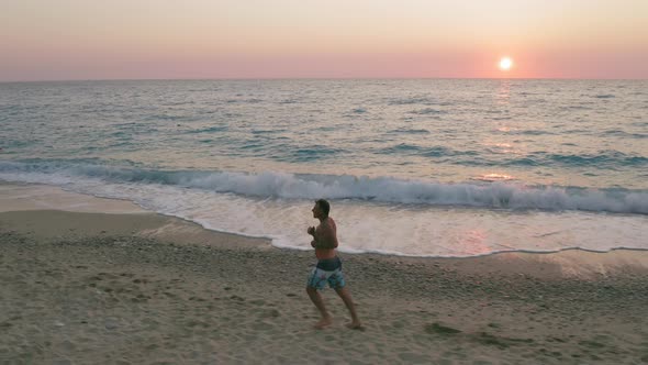 Aerial Low Altitude Side Follow View of Man Running Along the Beach in Sunset Golden Sunlight