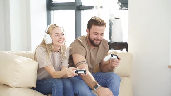 Happy Young Man and Woman Sitting on Sofa in Living Room Playing Computer Video Game