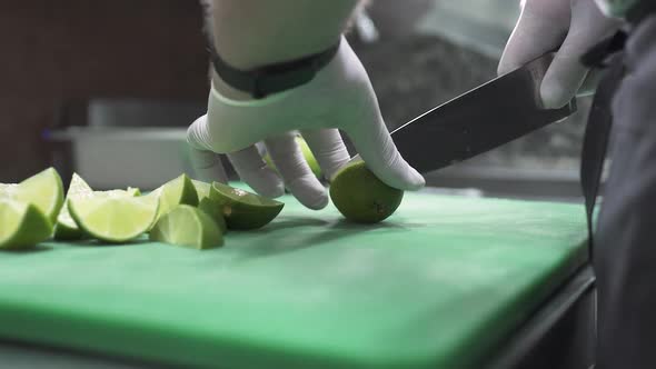 Chef in Gloves Cuts Fresh Lime Into Slices with Knife alt