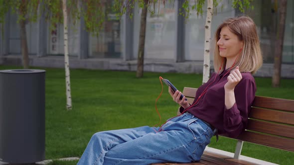 Woman Standing in the Town while Using Headphones to listen to Music. alt