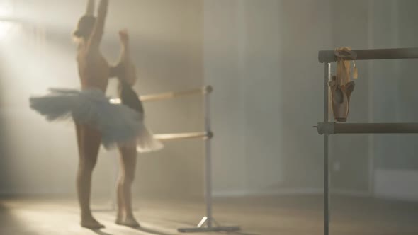 Golden Pointes Hanging on Barre with Blurred Teacher Explaining Ballet Movement for Student at alt