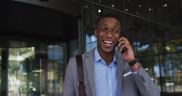 Smiling african american businessman using smartphone outside of modern office building alt