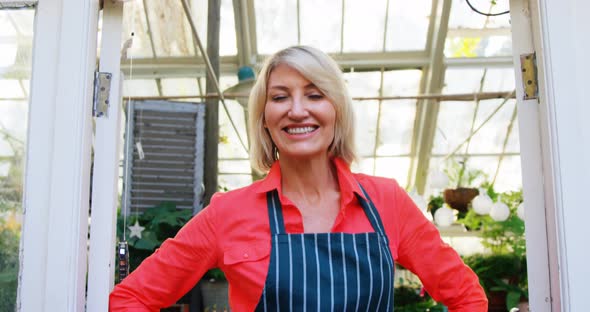 Mature woman standing at the entrance of greenhouse alt