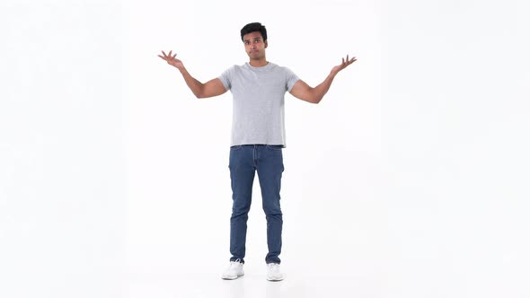 Young Indian man in plain blue jeans and grey t-shirt shrugging his shoulder