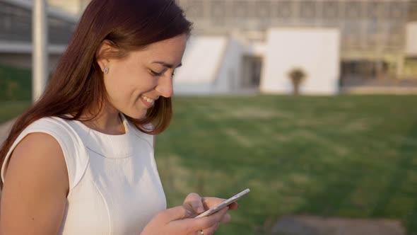 Side View of Smiling Redhead Woman Typing on Smartphone alt