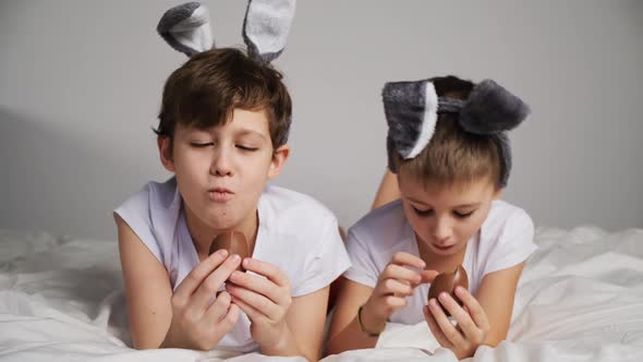 Two Kids with Rabbit Ears Eat Easter Eggs Lying in Bed alt