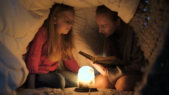 Mom and Daughter Sitting Under Blanket and Reading alt
