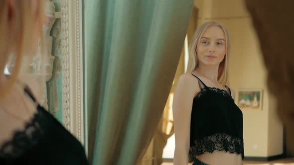 Young woman with blue eyes and blonde hair looking at her reflection in mirror alt