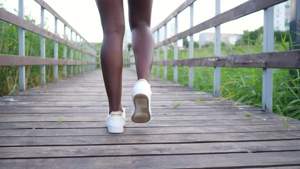 African-American Woman in White Sneakers Walks Along Bridge alt