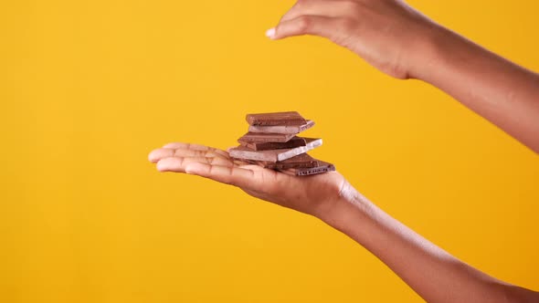 Holding Stack of Chocolate Against Yellow Background alt