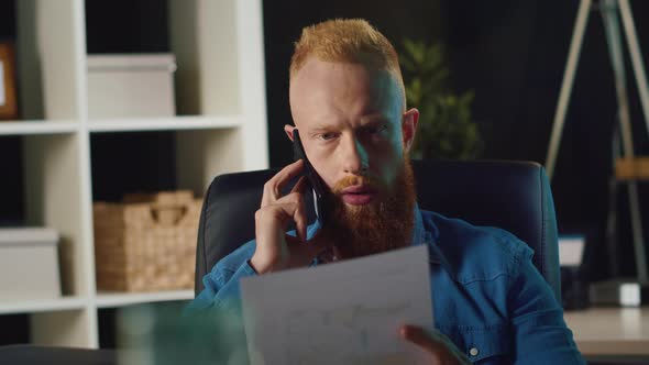 Hipster Man Talking Smartphone Indoors. Businessman Checking Document at Work. alt