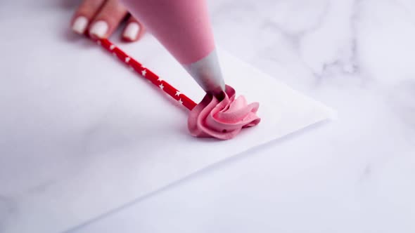 Meringue in the form of a pink cap is squeezed out of a pastry bag on a piece of parchment on a stic