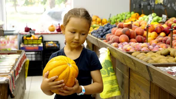 Kid Girl with Ripe Melon is Walking Along Grocery Rows Toward to Cashier