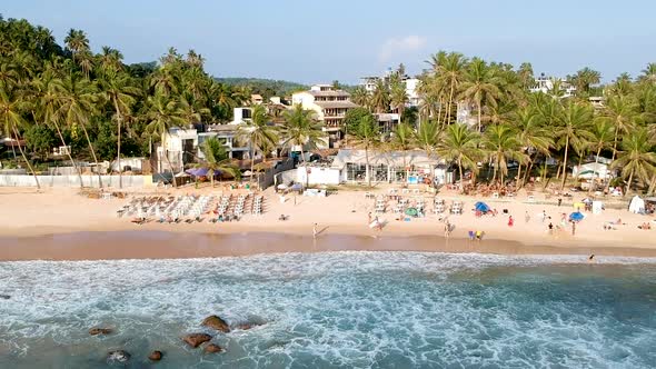 Aerial drone pan along busy Sri Lank beach at sunset golden hour. Mirissa Beach bar, Sri Lanka alt