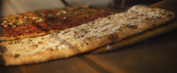 Delicious al taglio pizzas with different toppings being placed on a wooden surface in a pizza cafe. alt
