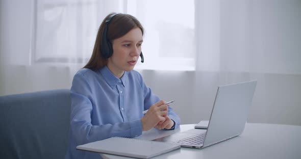 Female Specialist of Call-center Is Talking By Headset and Looking at Display of Laptop, Portrait alt