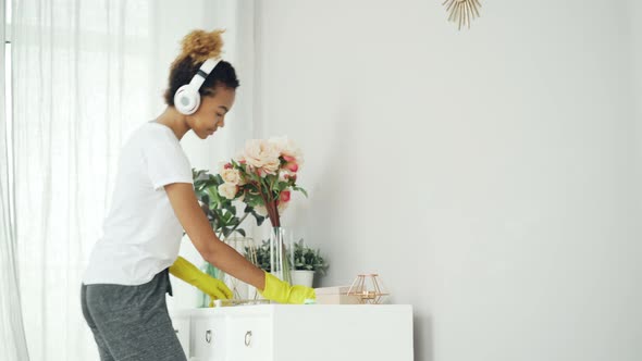 Attractive African American Housemaid Is Cleaning the House Dusting the Furniture and Listening To alt