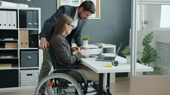 Businesswoman in Wheelchair Talking to Coworker in Office Discussing Business alt