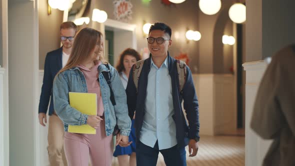 Joyful Multicultural Student Couple Talking Walking on College Corridor alt