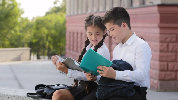 Two Hispnic Children Students Pupils Sitting Outdoors with Books Reading After Class alt