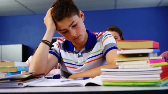 Thoughtful schoolboy sitting in classroom alt