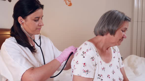 Doctor Checking Senior Woman Lungs with Stethoscope at Home