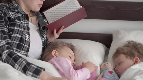 Authentic Cute Young Woman or Babysitter Reads Fairy Tale From Book to Children Before Bedtime alt