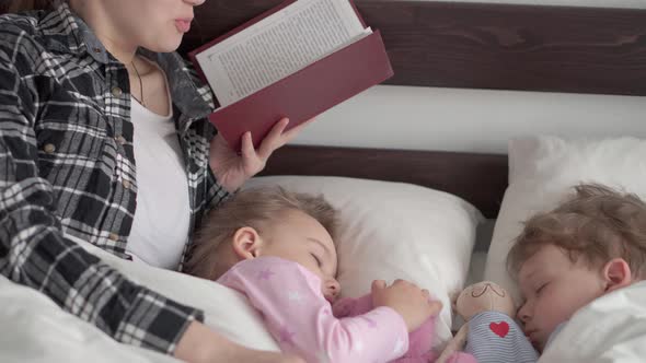 Authentic Cute Young Woman or Babysitter Reads Fairy Tale From Book to Children Before Bedtime