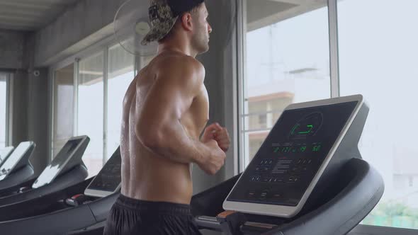 Muscular shirtless man running on treadmill at gym