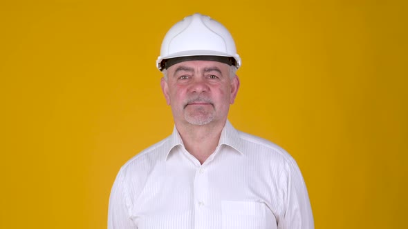 Portrait of Senior man builder in helmet posing on yellow background.