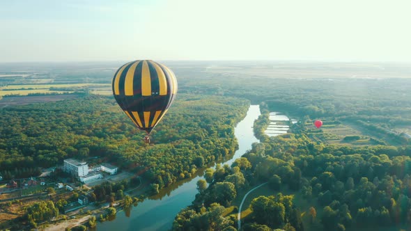 Aerial View of a Hot Air Balloon Flies Over the Trees Along the River. Fantastic Summer Sunset Scene alt
