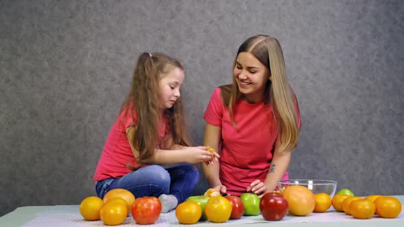 Happy woman eating orange with daughter at table alt
