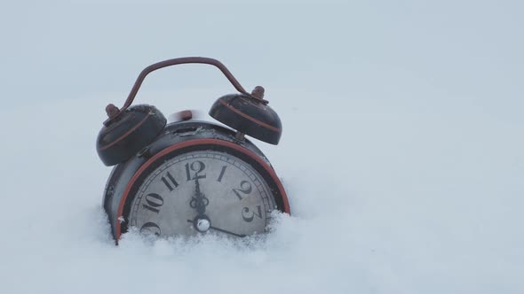 An old alarm clock rings at twelve o'clock, standing in the snow. alt
