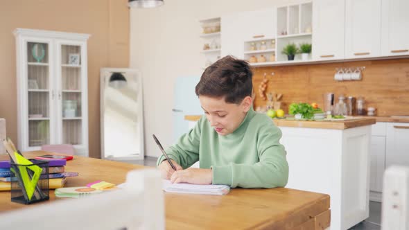 Boy In Kitchen Doing Homework And Chatting with Laptop on the Table alt
