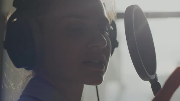 A Young Girl in Monitor Headphones in Front of a Microphone Records a Podcast alt