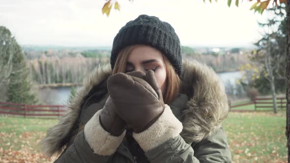 Front view of adult girl drinking hot beverage in cold windy autumn day. alt