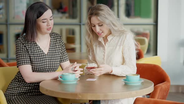 Two Charming Cheerful Young Women Scanning QR Code on Restaurant Table and Talking alt