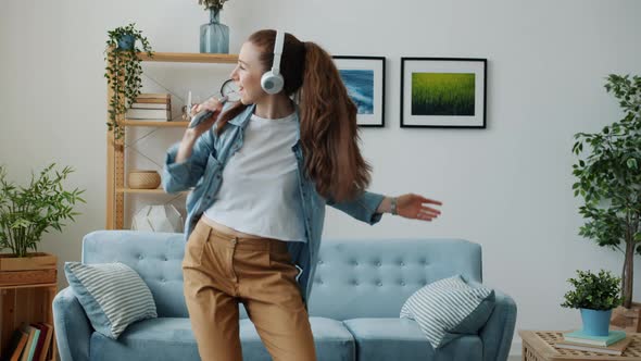 Cute Young Lady Wearing Headphones Dancing and Singing in Remote Control at Home alt