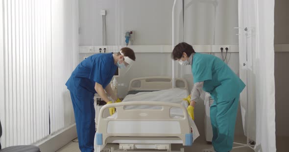 Medical Workers in Safety Mask and Gloves Changing Bed Sheets in Hospital Room alt